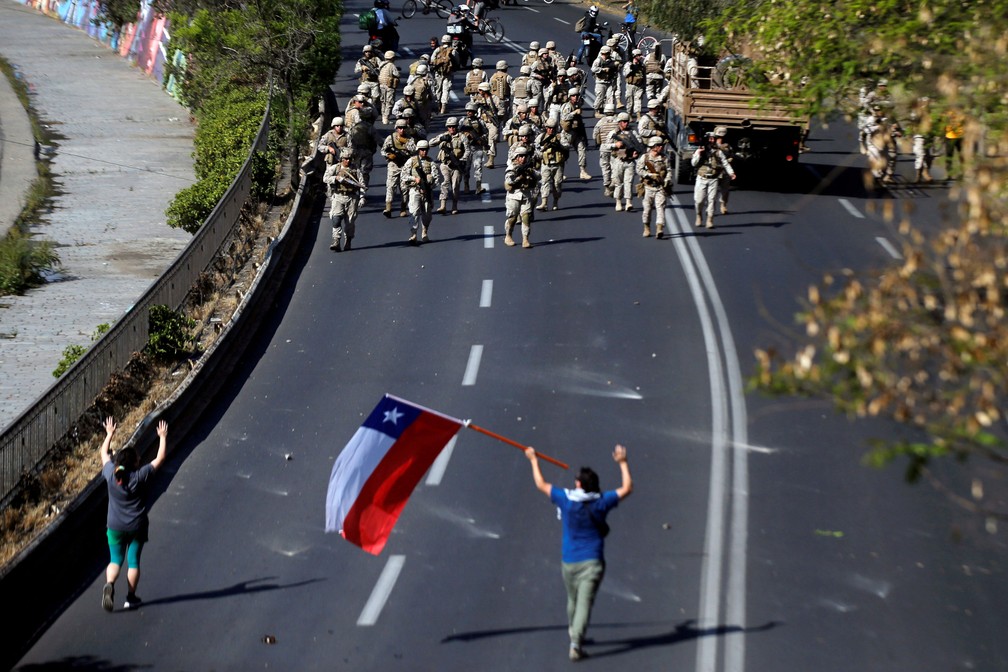 Manifestante com bandeira chilena caminha na direção de soldados chilenos durante protesto no domingo (20)  — Foto: Edgard Garrido / Reuters