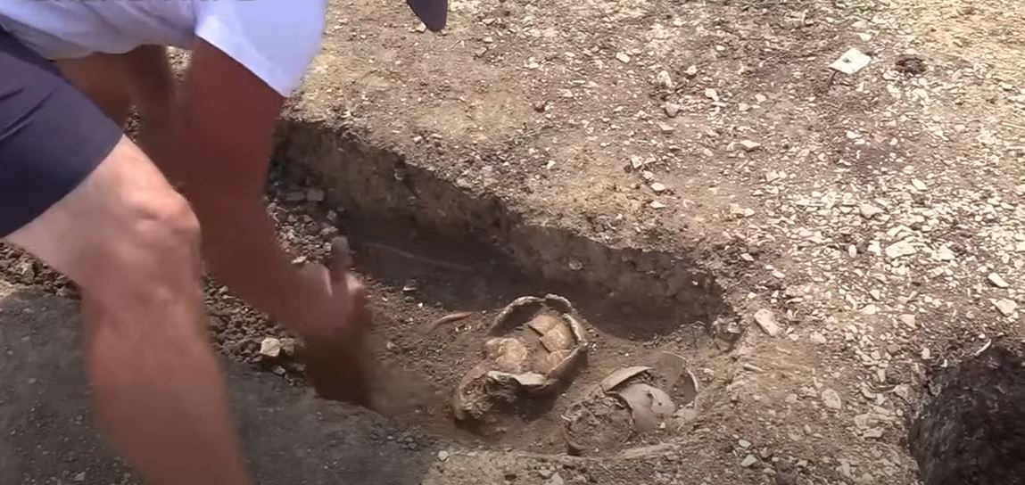 Arqueólogo investiga ossada encontrada em cemitério na Romênia (Foto: Gherla INFO/Youtube/Reprodução)