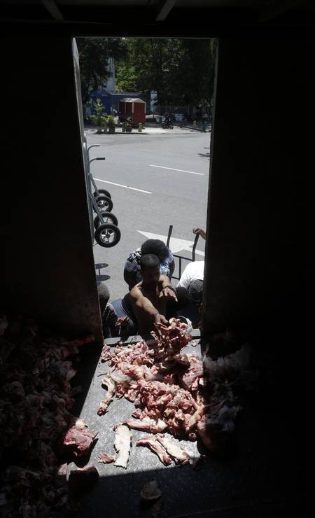 Mulheres, homens e jovens se amontoam em busca dos restos da carne e dos ossos. O que antes pediam para cachorros, agora pedem para comer.  — Foto: Domingos Peixoto / Agência O Globo