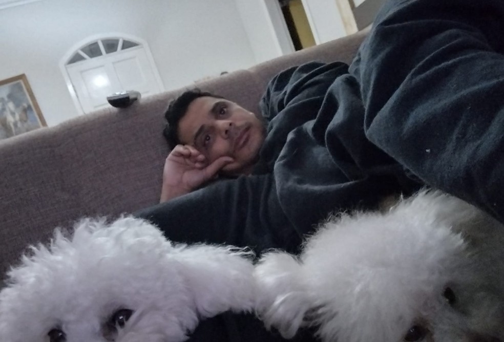 Denílson deitado no sofá da casa dele com suas cachorras se preparando para acompanhar as Olimpíadas. — Foto: Arquivo pessoal