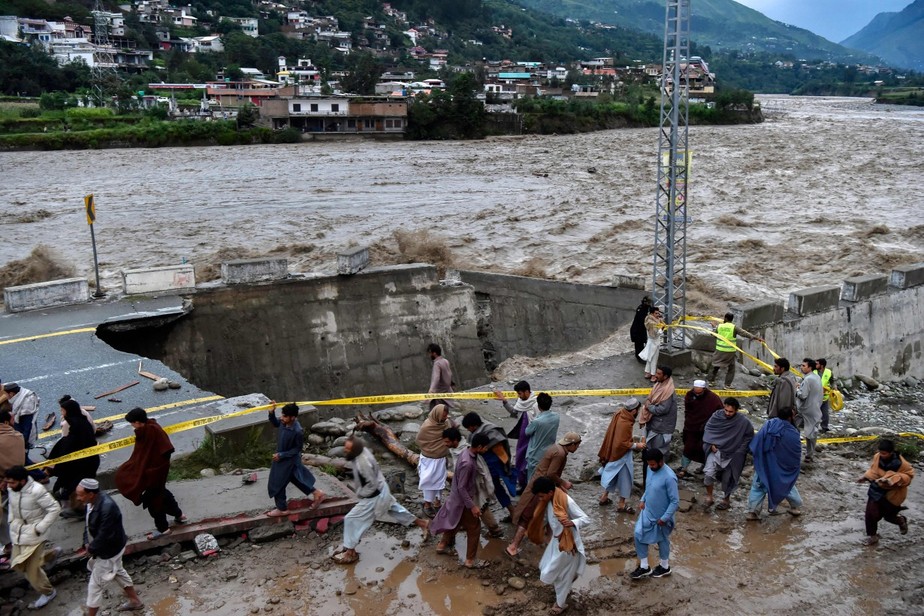 Pessoas se reúnem em frente a uma estrada danificada por inundações após fortes chuvas de monção na área de Madian, no vale do Swat, no Norte do Paquistão