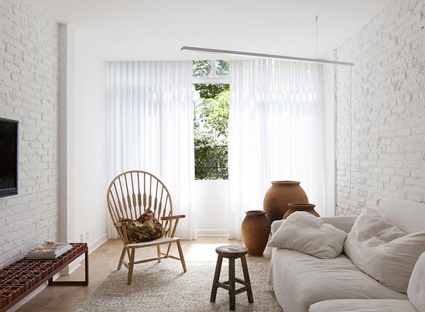 sala-sofa-tv-janela-branco-neutro-tijolos-aparentes-cortina-poltrona (Foto: Djan Chu/Divulgação)