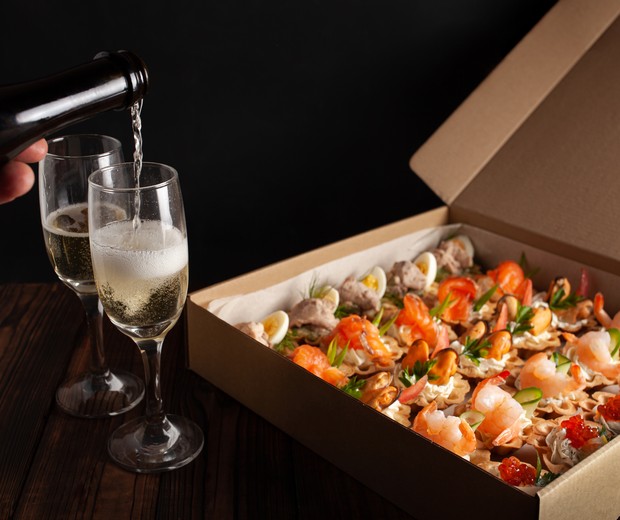 Champagne, tartlets, seafood salads. Cardboard box with food with home delivery. Gift box for holiday, party, family dinner. Catering. Delicious snacks. (Foto: Getty Images/iStockphoto)