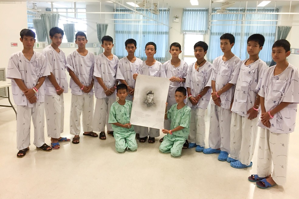 No Hospital Chiang Rai Prachanukroh, em Chiang Rai, os 12 meninos resgatados posam para foto com um desenho de Samarn Kunan, ex-mergulhador da Marinha tailandesa que morreu trabalhando para resgatá-los  (Foto: Chiang Rai Prachanukroh Hospital AND Ministry of Public Health/Handout via REUTERS )
