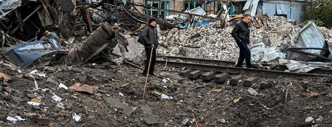 Pessoas são vistas perto de uma cratera causada por um ataque de mísseis perto de um pátio ferroviário em Kharkiv, na Ucrânia. — Foto: SERGEY BOBOK / AFP