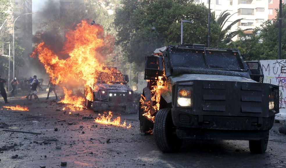 Veículos blindados da polícia foram incendiados em confronto neste domingo (18) em Santiago — Foto: Esteban Felt/AP