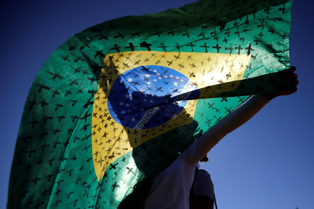 14 de julho - Manifestante segura bandeira do Brasil pintada com cruzes para simbolizar as mortes de Covid-19, durante protesto em Brasília — Foto: Adriano Machado/Reuters
