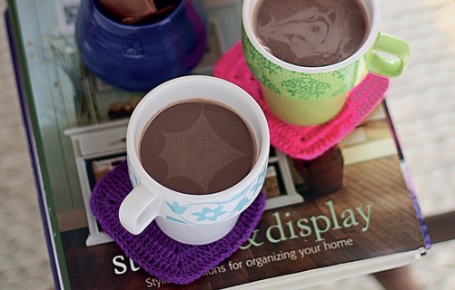 Para esquentar e adoçar a alma, chocolate quente com rum em xícaras apoiadas em porta-copos de crochê feitos por Ciça Cordeiro