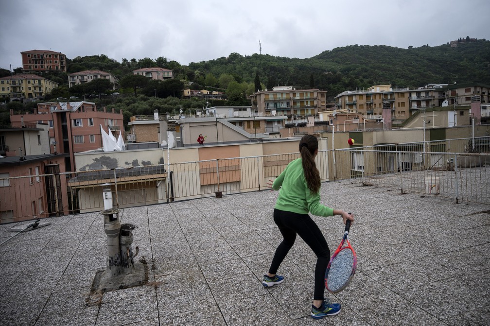 Vittoria Oliveri, de 13 anos, joga tênis com sua amiga Carola, de 11, nos telhados de sua casa em Finale Ligure, região da Ligúria, no noroeste da Itália, durante o isolamento do país com o objetivo de impedir a propagação da pandemia de COVID-19  — Foto:  Marco Bertorello/AFP