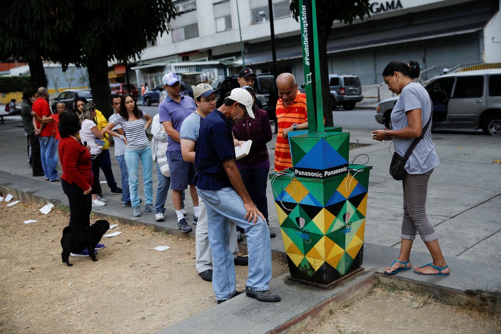 Venezuelanos tentam carregar celular utilizando painel solar — Foto: Reuters