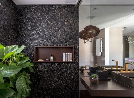 Banheiro da suíte principal projetada pelo escritório Tria Arquitetura tem boxe revestido de pedra escura e plantas