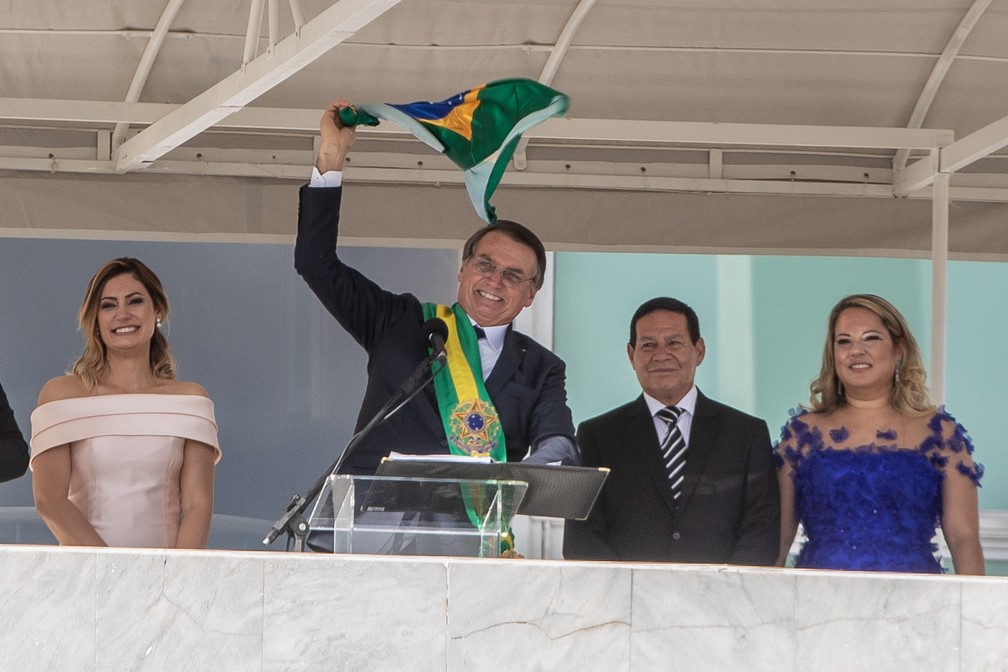 O novo presidente do Brasil, Jair Bolsonaro, gira no ar uma bandeira do Brasil ao lado de sua esposa, Michelle Bolsonaro, após receber a faixa presidencial do ex-presidente Michel Temer, no Palácio do Planalto, em Brasília — Foto: Fábio Tito/G1