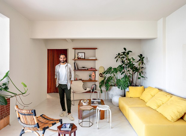 O morador, Rogério Gurgel, está na sala de estar. Desenhado por ele, o sofá fica ao lado de vasos de plantas (Foto: Fran Parente / Divulgação)