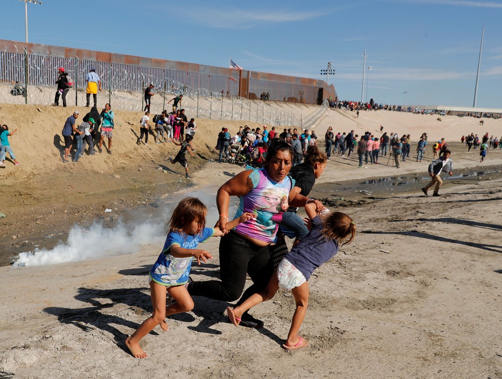 Mulher puxa crianÃ§as para longe do gÃ¡s lacrimogÃªneo atirado para dispersar migrantes de uma caravana da AmÃ©rica Central em Tijuana, diante do muro que separa o MÃ©xico do territÃ³rio americano, no dia 25 de novembro â Foto: Kim Kyung-Hoon/Reuters