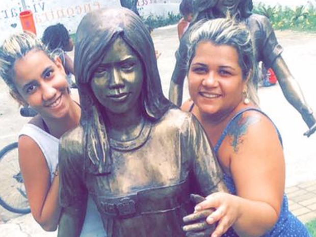 Kelly Guedes, à direita, com a irmã e a estátua que representa Géssica, que perderam no massacre da Escola Tasso da Silveira (Foto: Kelly Guedes/ Arquivo pessoal)