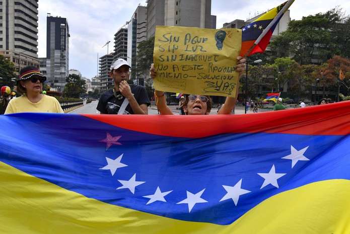 Manifestantes levam bandeira da Venezuela e cartazes em protesto em Caracas contra apagões no país — Foto: Yuri Cortez/AFP