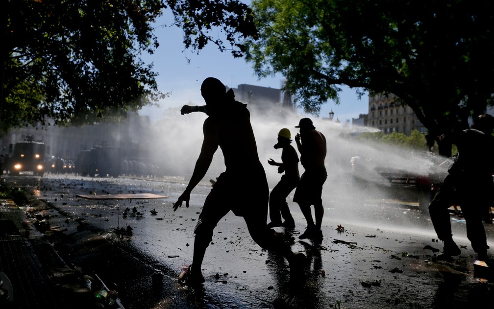 Manifestantes recebem jatos de água disparados pela polícia durante protesto contra a reforma da previdência em Buenos Aires, na Argentina, na segunda-feira (18) (Foto: AP Photo/Victor R. Caivano)