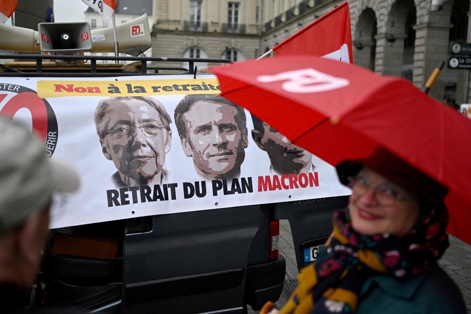Uma manifestante em frente a um cartaz com os rostos do presidente Emmanuel Macron e da premier Elisabeth Borne