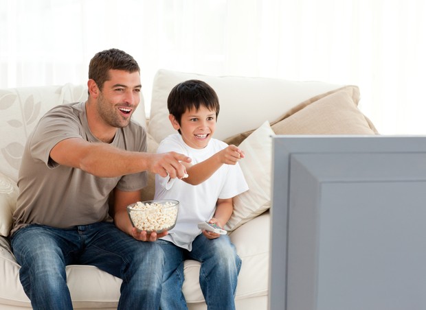 Homem assistindo televisão com criança (Foto: Shutterstock)