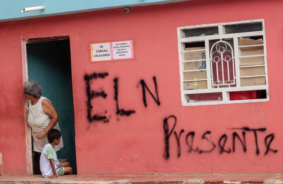 Moradores são vistos do lado de fora de uma casa com um grafite que diz 'ELN Presente' no bairro de Parada, na fronteira entre Colômbia e Venezuela