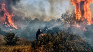 Um bombeiro tenta conter incêndio na área de Agioi Theodori, próximo à Atenas, na Grécia. As autoridades de saúde soaram alarmes da América do Norte à Europa e Ásia, pedindo às pessoas que se mantenham hidratadas e protegidas do sol escaldante, em um lembrete dos efeitos do aquecimento global. — Foto: Valerie GACHE / AFP