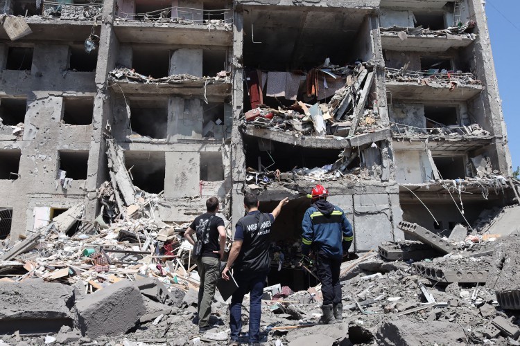 Um investigador de crimes de guerra e integrantes de uma equipe de resgate observam prédio destruído por ataque de míssil russo — Foto: OLEKSANDR GIMANOV/AFP