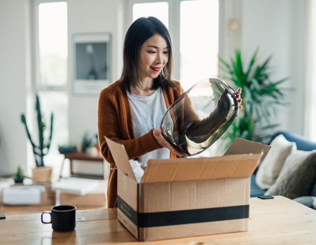 Smiling young Asian woman unpacking a carton box, excited to see her online purchase. Online shopping makes life easier. Small business concept. (Foto: Getty Images)