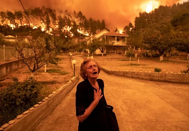 Uma idosa grita quando um incêndio se aproxima de sua casa na vila de Gouves, na ilha de Evia, Grécia, em 8 de agosto de 2021 (Foto: KONSTANTINOS TSAKALIDIS PARA BLOOMBERG NEWS via BBC)