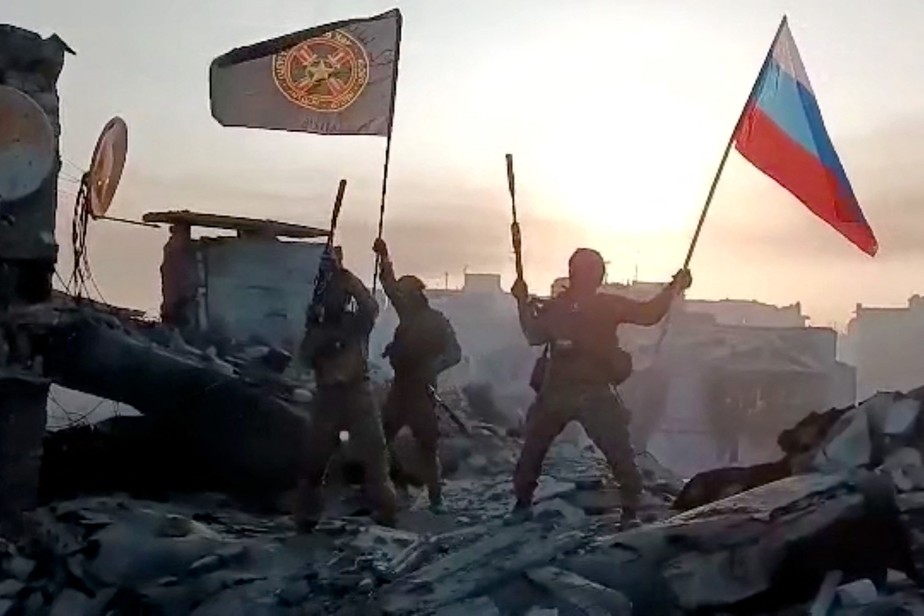 Soldados ligados ao Wagner mostram bandeiras russa e do grupo em Bakhmut.