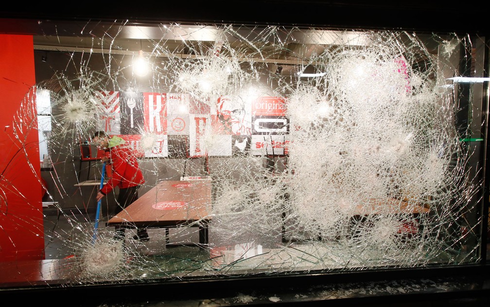 Homem limpa restaurante de fast food com janelas quebradas durante protesto contra toque de recolher em Roterdã, na Holanda, na segunda-feira (25) — Foto: AP Photo/Peter Dejong