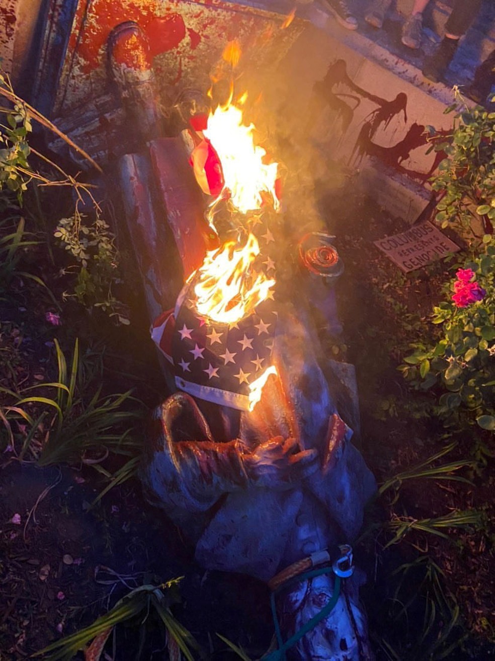 Estátua de Cristóvão Colombo é vista no chão, enrolada em uma bandeira em chamas, após ser retirada do pedestal por manifestantes, em Richmond, Virginia, na terça-feira (9) — Foto: Instagram/@Michaelahatton + @804RRJA/via Reuter
