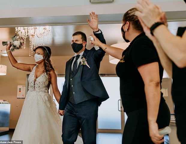 Casal com máscara comemora casamento, enquanto funcionário de hotel espera para limpar as mãos com um frasco de álcool gel, em Portugal (Foto: Valtar Antunes)