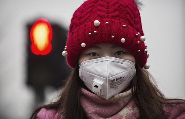 Jovem chinesa usa máscara para se proteger da poluição durante caminhada pelas ruas de Pequim. O governo emitiu um alerta vermelho, quando a capital atingiu o pior nível de poluição no ar em 8 de dezembro (Foto: Kevin Frayer/Getty Images)