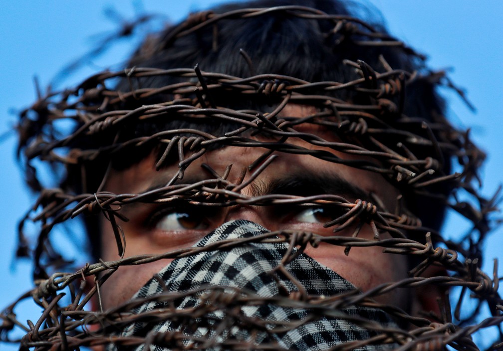 11 de outubro - Um homem da Caxemira utiliza uma máscara com a cabeça coberta de arame farpado em Srinagar, na Índia, enquanto assiste a um protesto após as tradicionais orações de sexta-feira com restrições após a retirada do status constitucional especial para a Caxemira pelo governo indiano  — Foto: Danish Ismail/Reuters