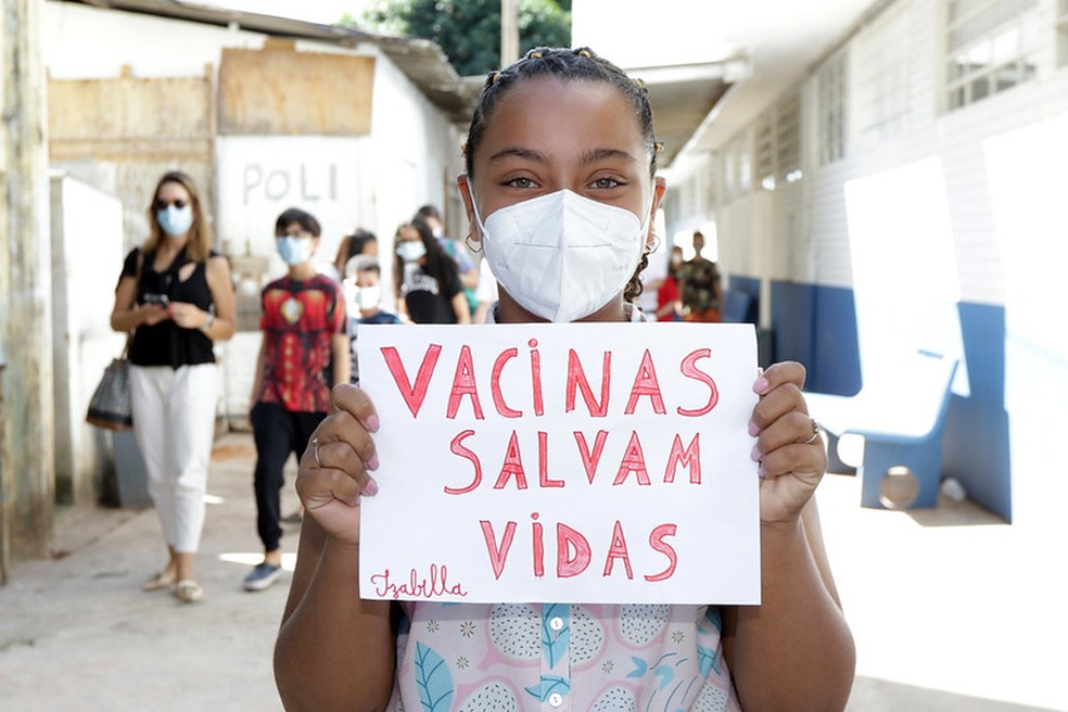 Menina segura cartaz onde se lê "Vacinas salvam vidas", durante campanha de  imunização contra Covid-19, no Distrito Federal — Foto: Sandro Araújo/Agência Saúde do DF