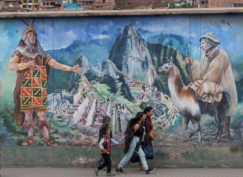 Uma família caminha ao lado de um mural da cidadela inca de Machu Picchu na cidade de Cusco, Peru