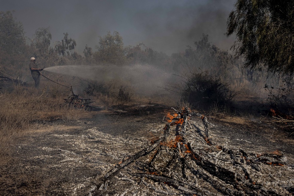 Um bombeiro israelense tenta apagar um incêndio causado por um balão incendiário lançado por palestinos na Faixa de Gaza, no lado israelense da fronteira entre Israel e Gaza, no domingo (16) — Foto: Tsafrir Abayov/AP