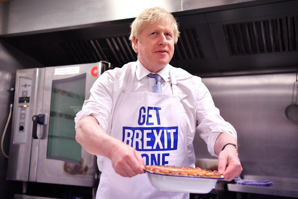 Boris Johnson prepara uma torta em uma cozinha em Derby, na Inglaterra, em dezembro, com um avental que diz 'realize o Brexit'. — Foto: Ben Stansall / AFP / Pool