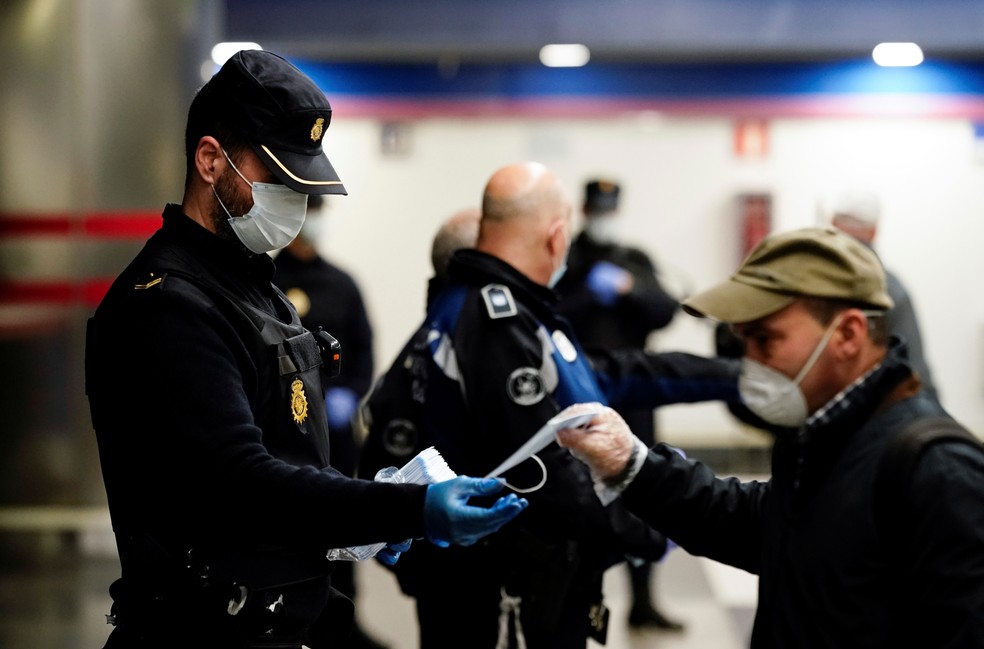 Policial dá máscaras protetoras gratuitas em uma estação de metrô em Madri, na Espanha, nesta segunda-feira (13) — Foto:  Juan Medina/ Reuters
