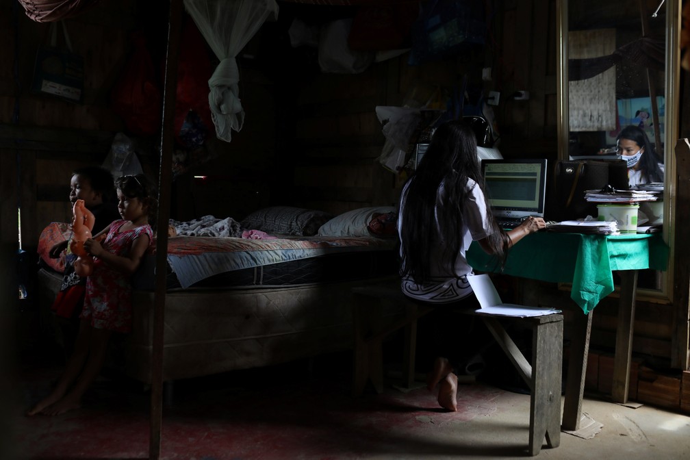 Vanda trabalha no computador enquanto sua sobrinha Maria e seu sobrinho Davi assistem TV no mesmo cômodo — Foto: Bruno Kelly/Reuters