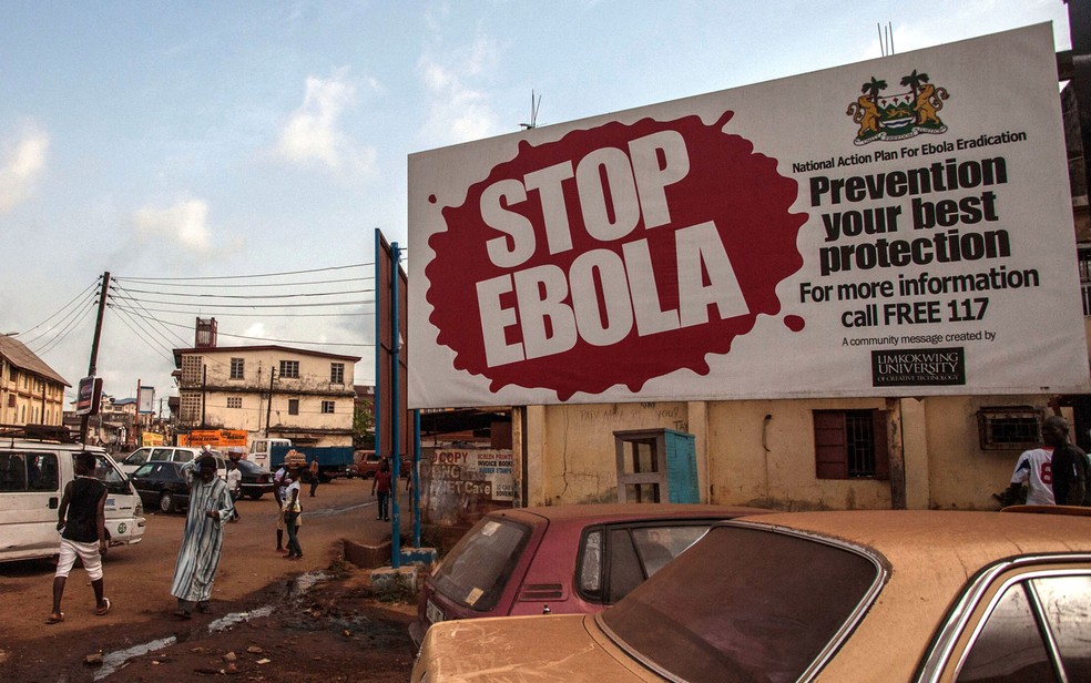 Pessoas passam por outdoor com alerta sobre o ebola na cidade de Freetown, em Serra Leoa, em 2016 — Foto: Aurelie Marrier d'Unienville/AP