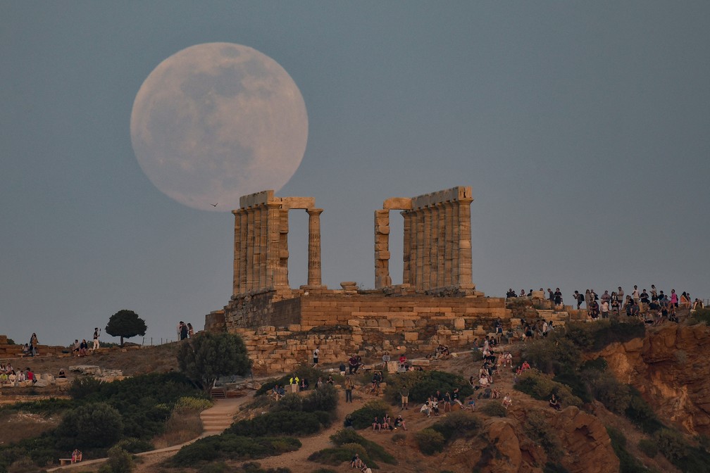 Grécia: moradores e turistas no Templo de Poseidon observam a lua cheia nascendo — Foto: Louisa Gouliamaki/AFP