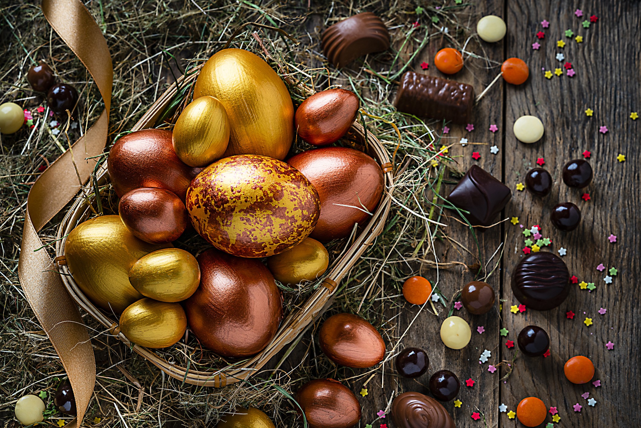 Holidays: hand painted gold and bronze colored Easter eggs in a wicker basket shot from above on rustic wooden table. The composition includes chocolate candies, sugar sprinkles and a gold colored ribbon. Predominant color is brown. High resolution 42Mp s (Foto: Getty Images)