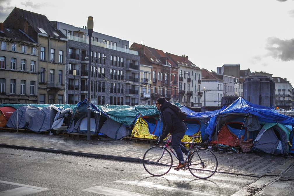 Um homem passa de bicicleta diante de um acampamento improvisado do lado de fora do centro de recepção Petit Chateau, em Bruxelas, Bélgica, terça-feira, 17 de janeiro de 2023. — Foto: Foto AP/Olivier Matthys