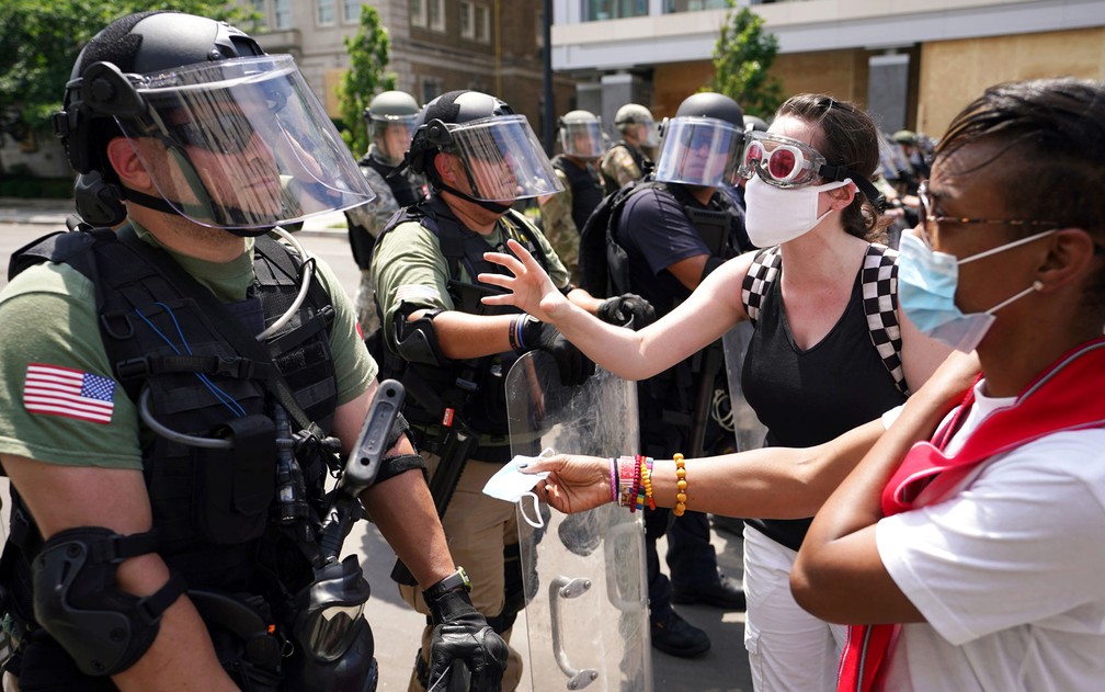 Manifestante oferece máscara de proteção a policial, perto da Casa Branca, em Washington, na quarta-feira (3) — Foto: Reuters/Kevin Lamarque 