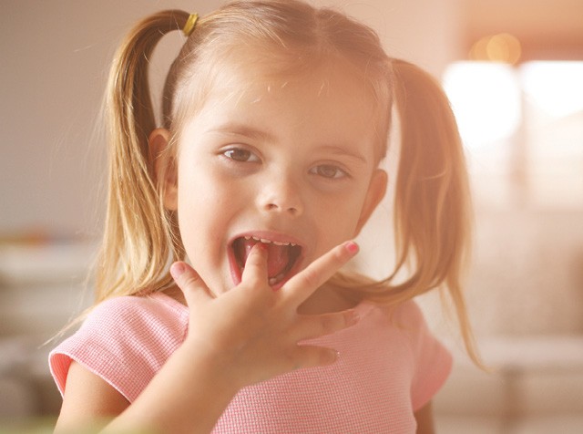 Menina loira de chiquinhas lambendo os dedos (Foto: thinkstock)