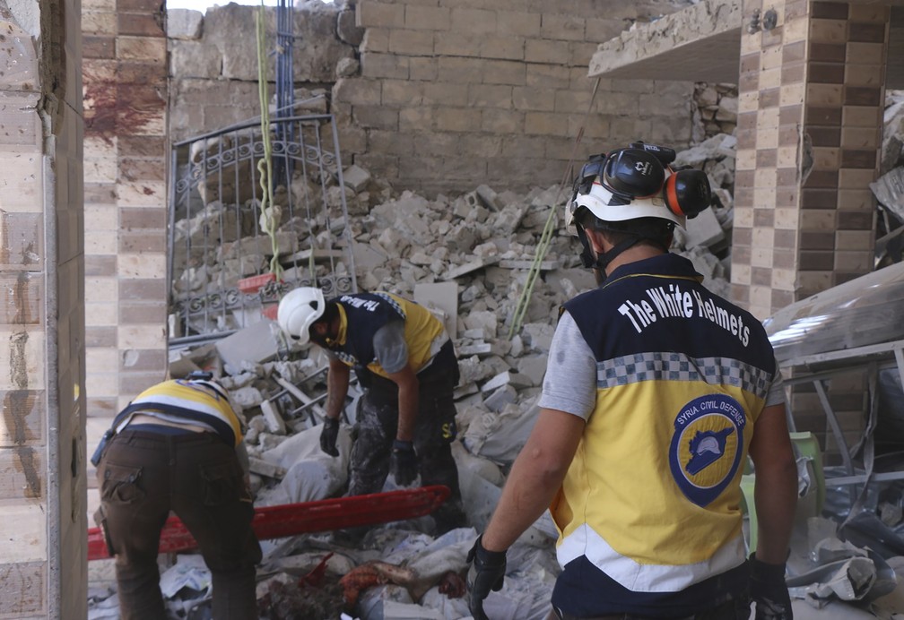 Membros dos Capacetes Brancos da Síria procuram vítimas em prédio destruído por ataques nesta segunda-feira (22), supostamente realizados pelo governo sírio ou pela Rússia. — Foto: Syrian Civil Defense White Helmets via AP