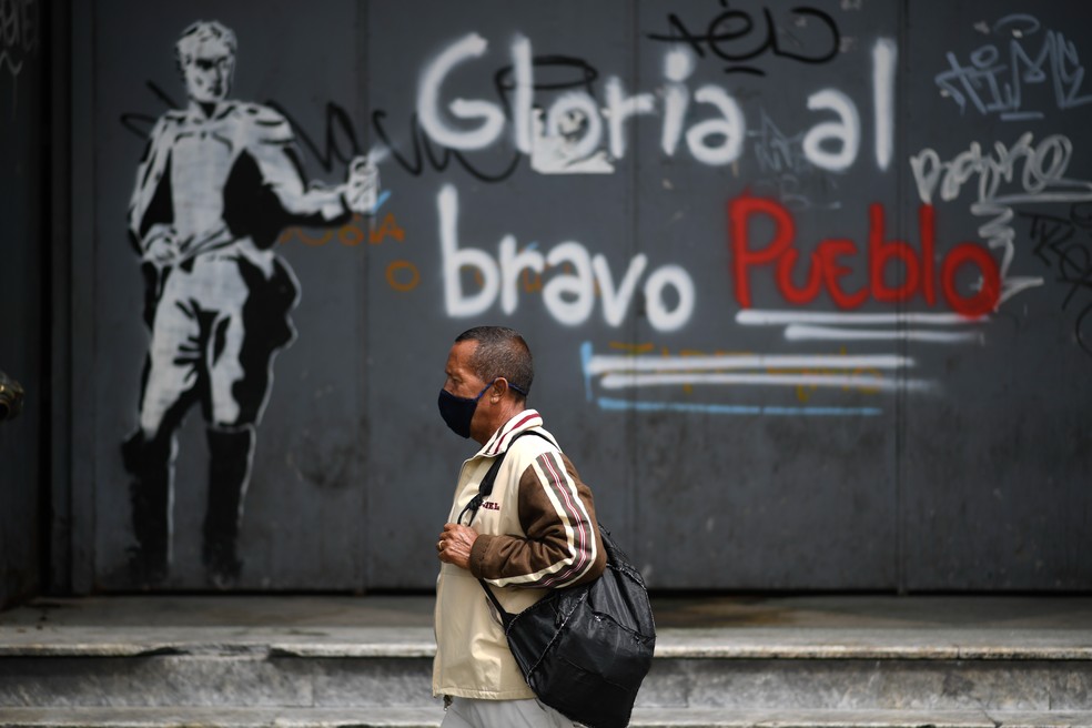 Um homem usando uma máscara facial passa por um grafite com a mensagem 'glória ao povo corajoso' no centro de Caracas, na Venezuela, depois que o governo impôs um bloqueio nacional como medida preventiva contra conter a Covid-19 — Foto: Federico Parra/AFP