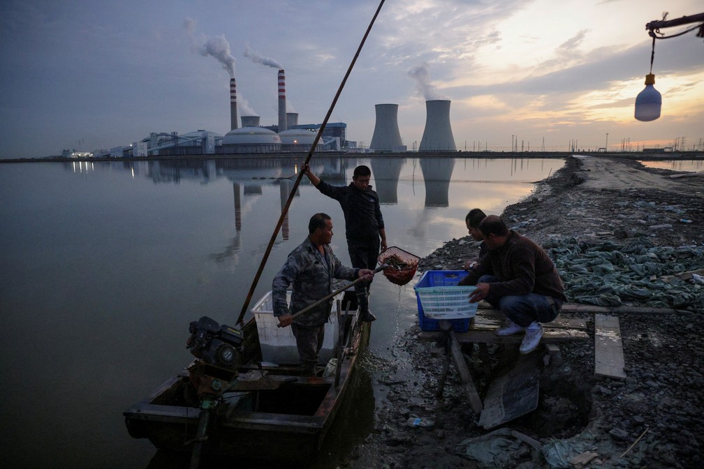 14 de outubro - Pescadores trazem sua pesca de um lago em frente a uma usina de energia nos arredores de Tianjin, na China  — Foto: Thomas Peter/Reuters/Arquivo