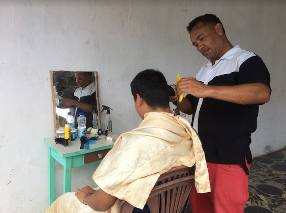 Com um espelho, uma banquinha e cadeiras de plástico, Gleomar improvisou um espaço embaixo do prédio onde mora para trabalhar como barbeiro, em Campina Grande — Foto: Érica Ribeiro/G1